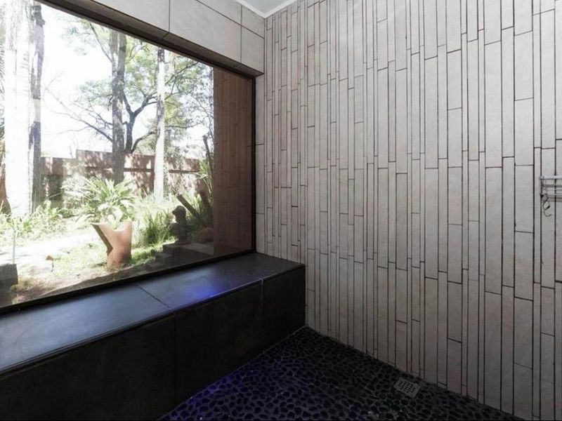 Modern bathroom featuring a unique pebble floor, vertical tiled wall, and a large window overlooking the garden, creating a serene and bright atmosphere.