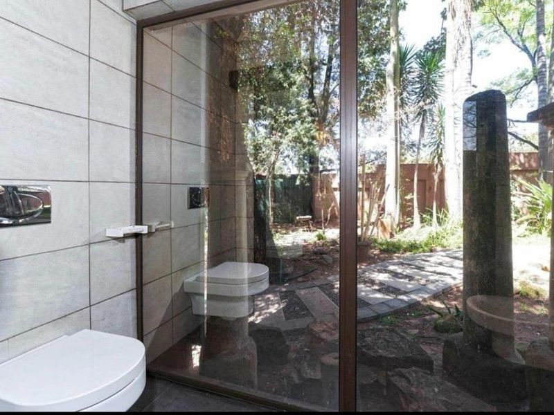 Modern bathroom featuring a wall-mounted toilet, sleek tiled finishes, and a large glass window offering a view of the garden.