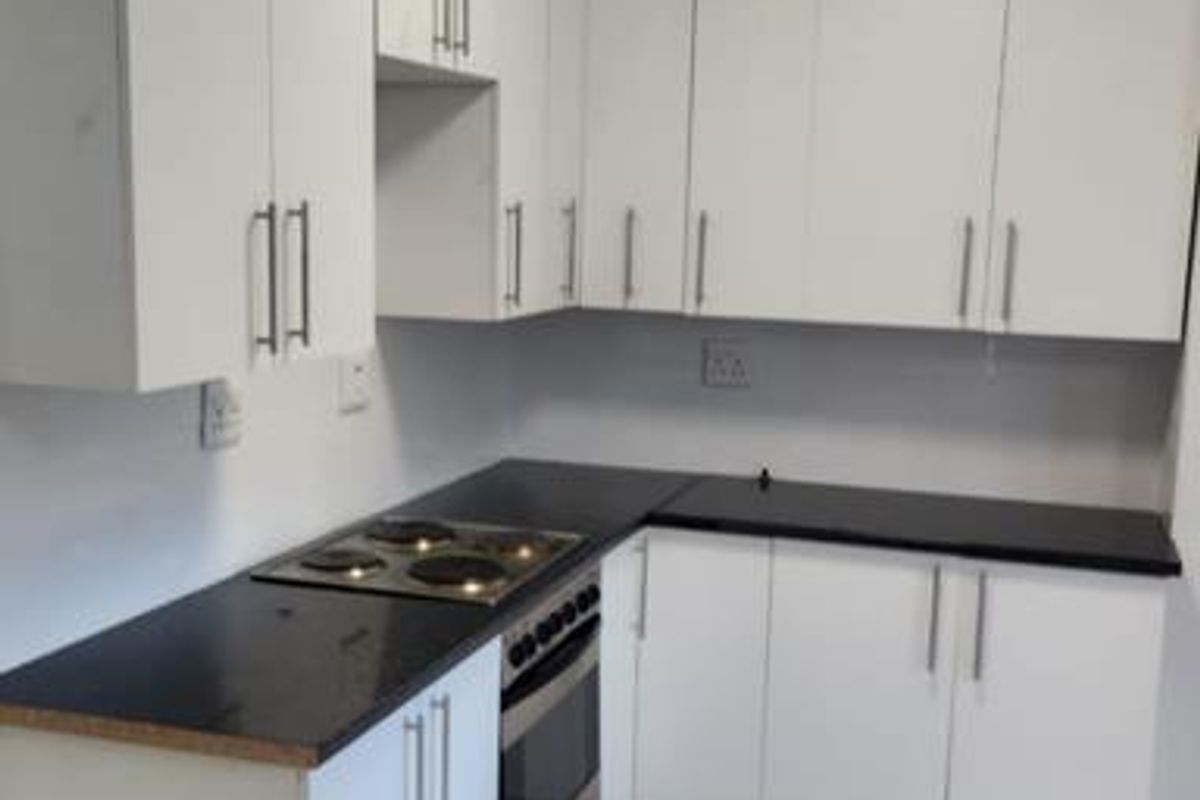 A functional kitchen featuring white cabinetry, black countertops, an integrated electric hob and oven, and tiled flooring.