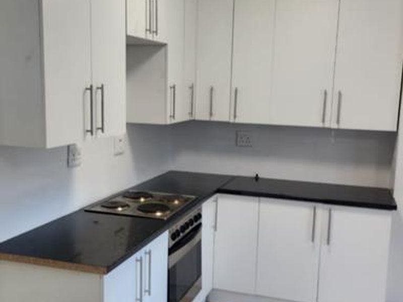 A functional kitchen featuring white cabinetry, black countertops, an integrated electric hob and oven, and tiled flooring.
