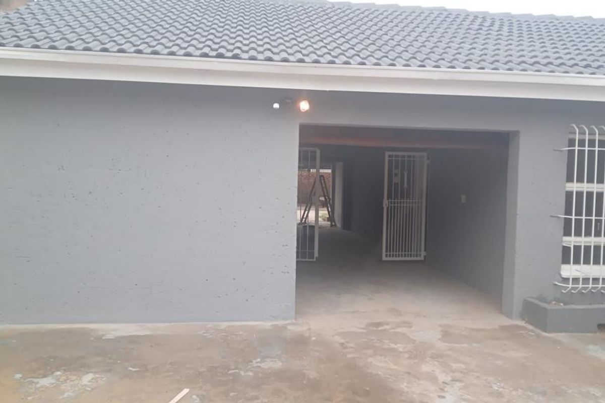 Rear exterior view of the property featuring a tiled roof, security gates, and security bars on the windows with a concrete driveway area.