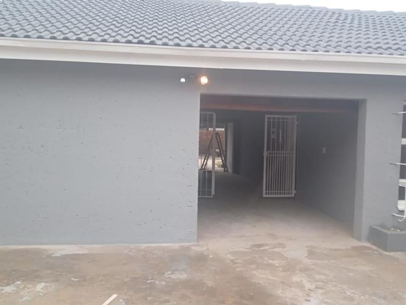 Rear exterior view of the property featuring a tiled roof, security gates, and security bars on the windows with a concrete driveway area.