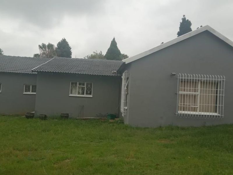 Rear view of the house featuring a tiled roof, painted exterior walls, and security bars on the windows, set against a large lawn area.