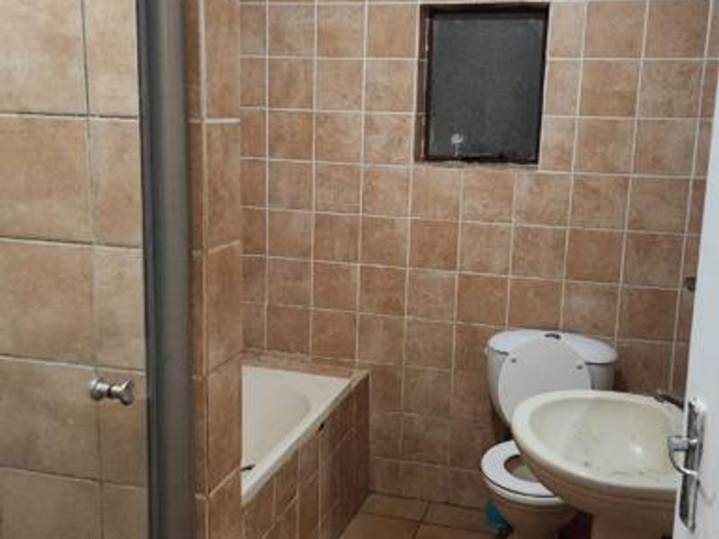 A dated bathroom featuring a bathtub, pedestal sink, toilet, and shower enclosure with full-height wall tiling and floor tiles.