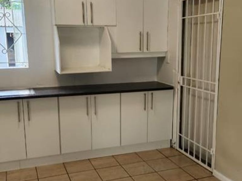 A functional kitchen area featuring white built-in cabinetry, dark countertops, and tiled flooring, with a security gate providing access to the exterior.