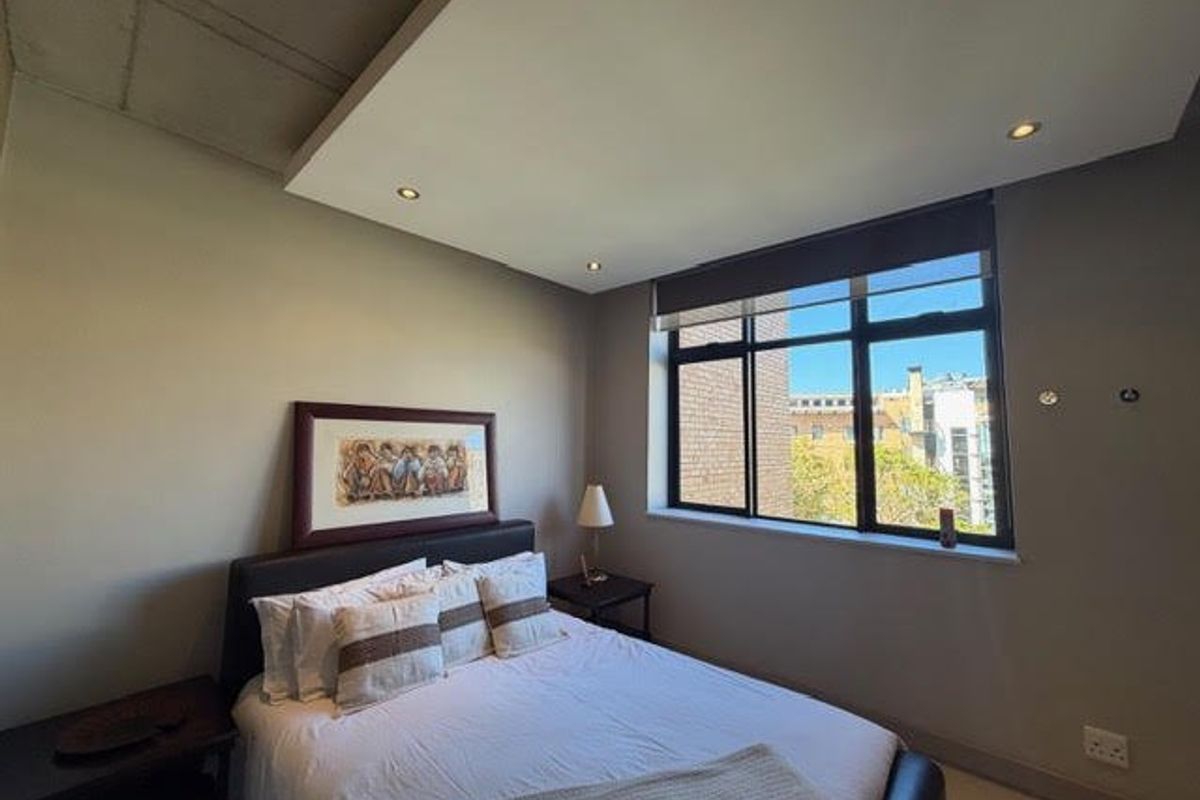 A well-lit bedroom featuring a modern drop ceiling with recessed lighting, large windows with roller blinds, and neutral wall finishes.