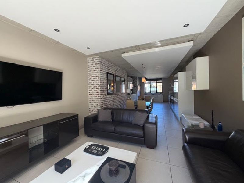 Spacious open-plan living and kitchen area featuring modern tiled floors, an exposed brick feature wall, and a contemporary exposed concrete ceiling design.