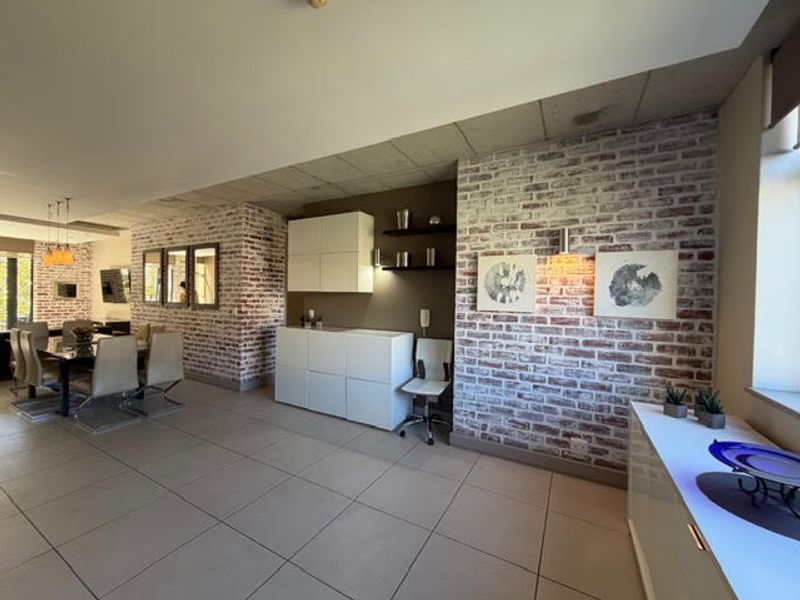 Spacious open-plan living and dining area featuring exposed brick walls, modern tiled flooring, and sleek built-in cabinetry with integrated shelving.