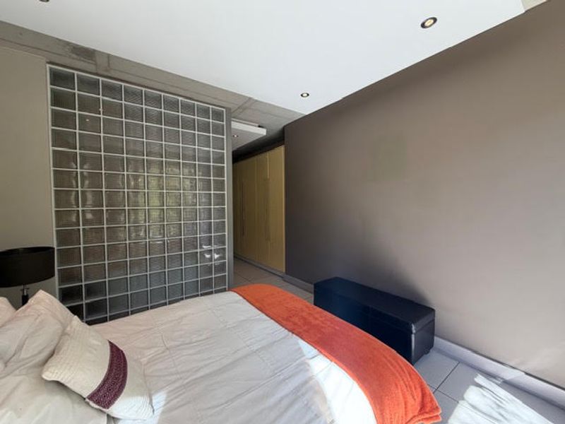 Modern bedroom featuring a unique glass block feature wall, built-in cabinetry, and an industrial-style exposed concrete ceiling with recessed lighting.