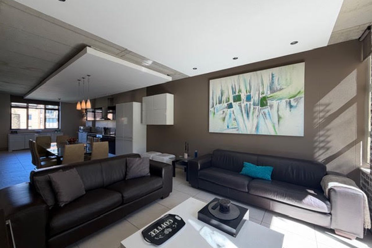 Spacious open-plan living and dining area featuring modern tiled floors, exposed concrete ceilings, and a sleek integrated kitchen layout.