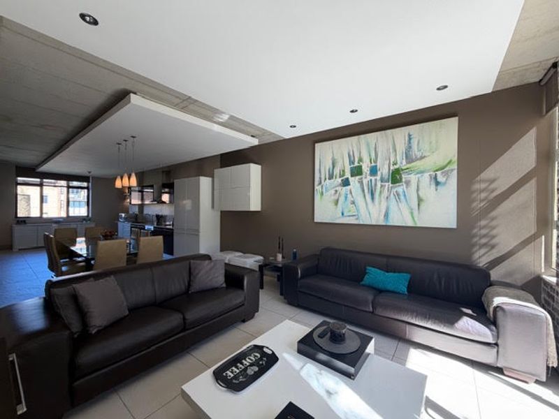 Spacious open-plan living and dining area featuring modern tiled floors, exposed concrete ceilings, and a sleek integrated kitchen layout.