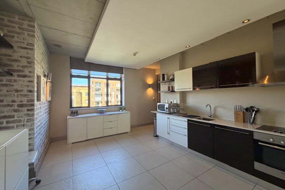 Modern open-plan kitchen featuring sleek two-tone cabinetry, exposed brick and concrete elements, and high-quality built-in appliances with ample natural light.