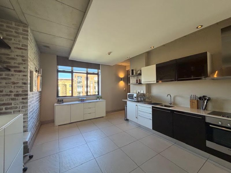 Modern open-plan kitchen featuring sleek two-tone cabinetry, exposed brick and concrete elements, and high-quality built-in appliances with ample natural light.