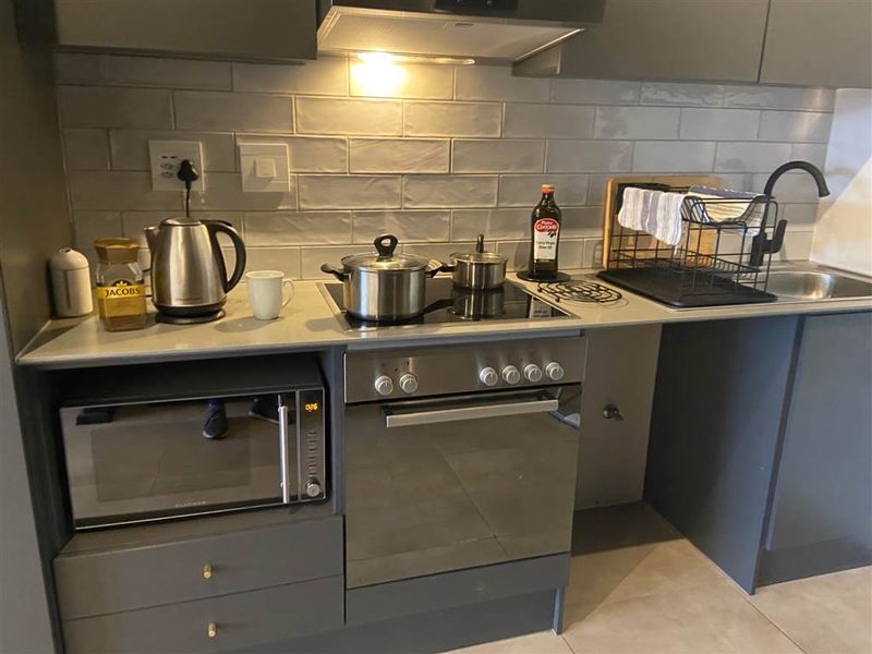 Modern kitchen featuring grey cabinetry, subway tile backsplash, integrated oven, electric hob, extractor fan, and a stainless steel sink with a mixer tap.