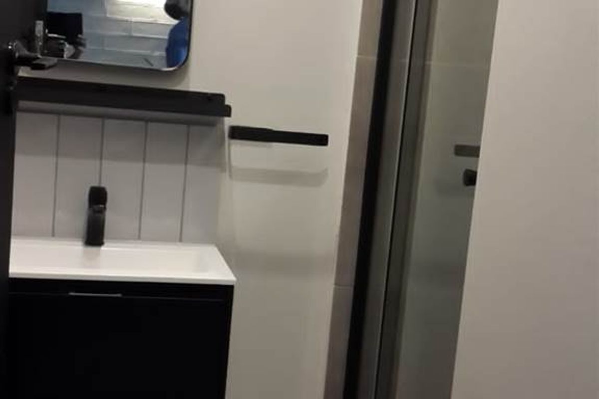 A modern bathroom featuring a wall-mounted vanity with a black basin mixer, tiled splashback, and a glass shower enclosure with a black frame.