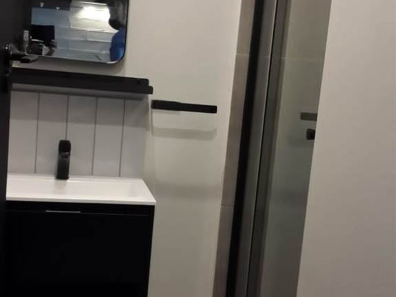 A modern bathroom featuring a wall-mounted vanity with a black basin mixer, tiled splashback, and a glass shower enclosure with a black frame.