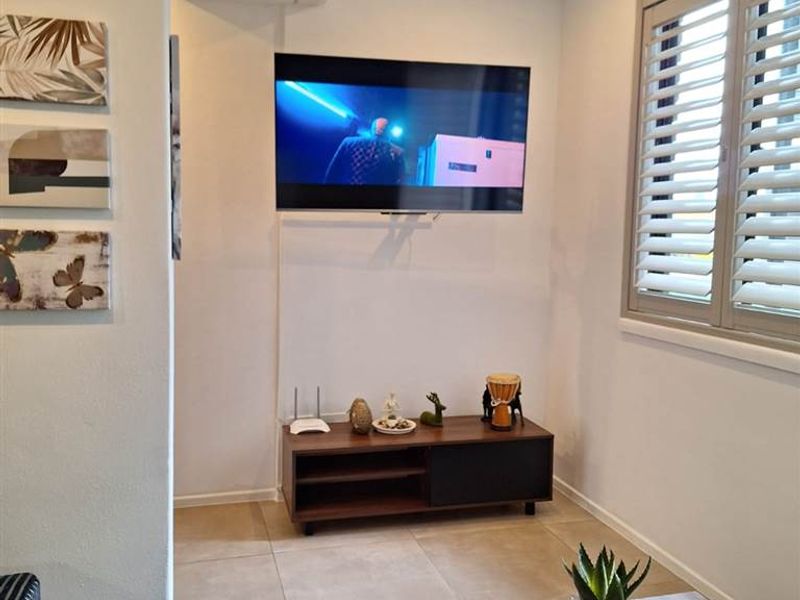 A well-maintained living area featuring neutral tiled flooring, recessed ceiling lighting, and adjustable plantation shutters for natural light control.