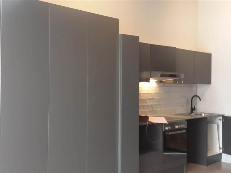 Modern compact kitchen featuring dark grey cabinetry, built-in oven, extractor fan, and a distinctive exposed brick wall finish.