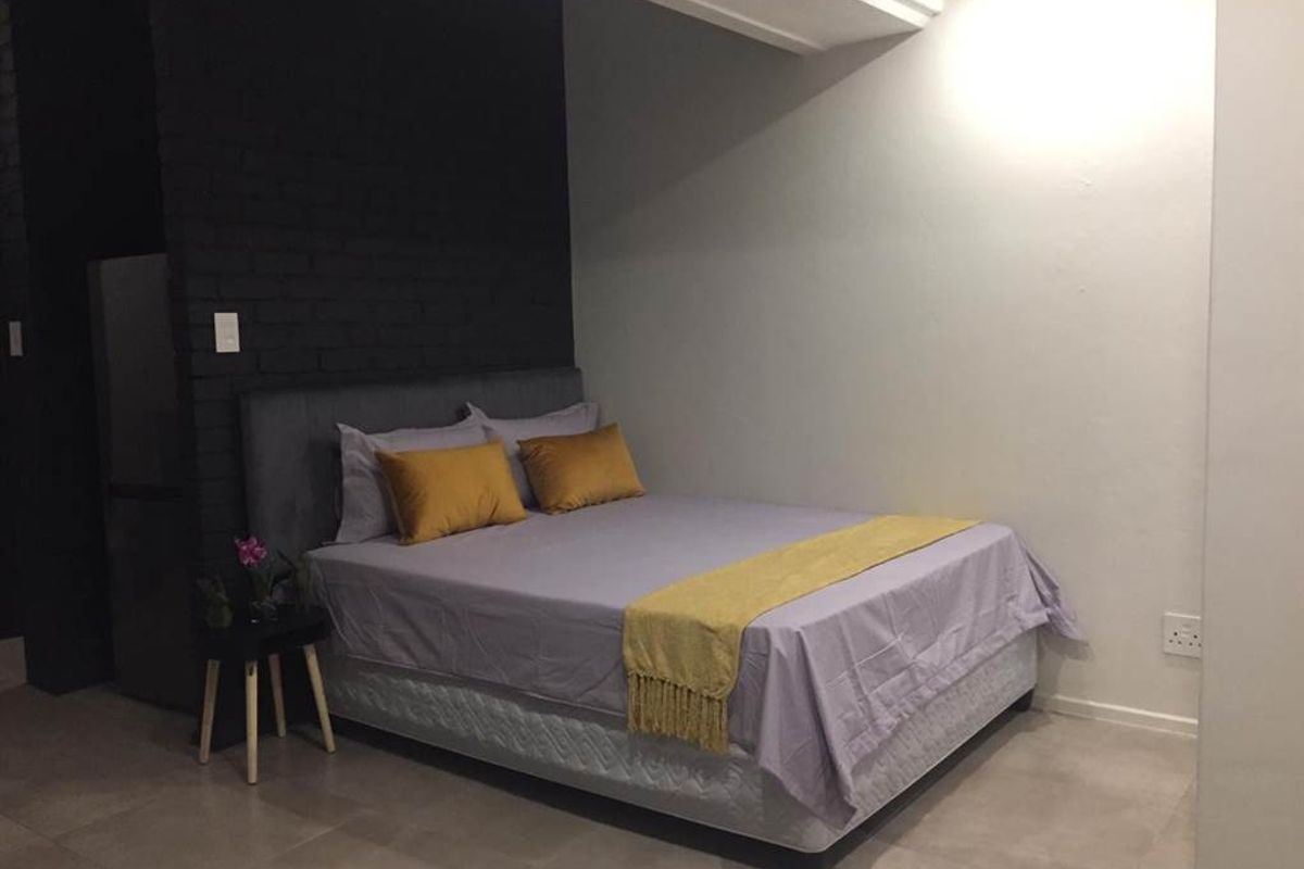 A bedroom featuring a dark painted exposed brick feature wall, neutral tiled flooring, and recessed ceiling lighting.