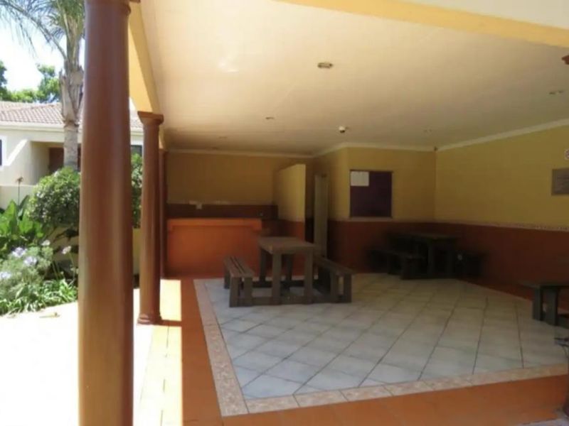 A covered outdoor patio area featuring tiled flooring, support columns, and a built-in counter, suitable for communal outdoor entertainment.