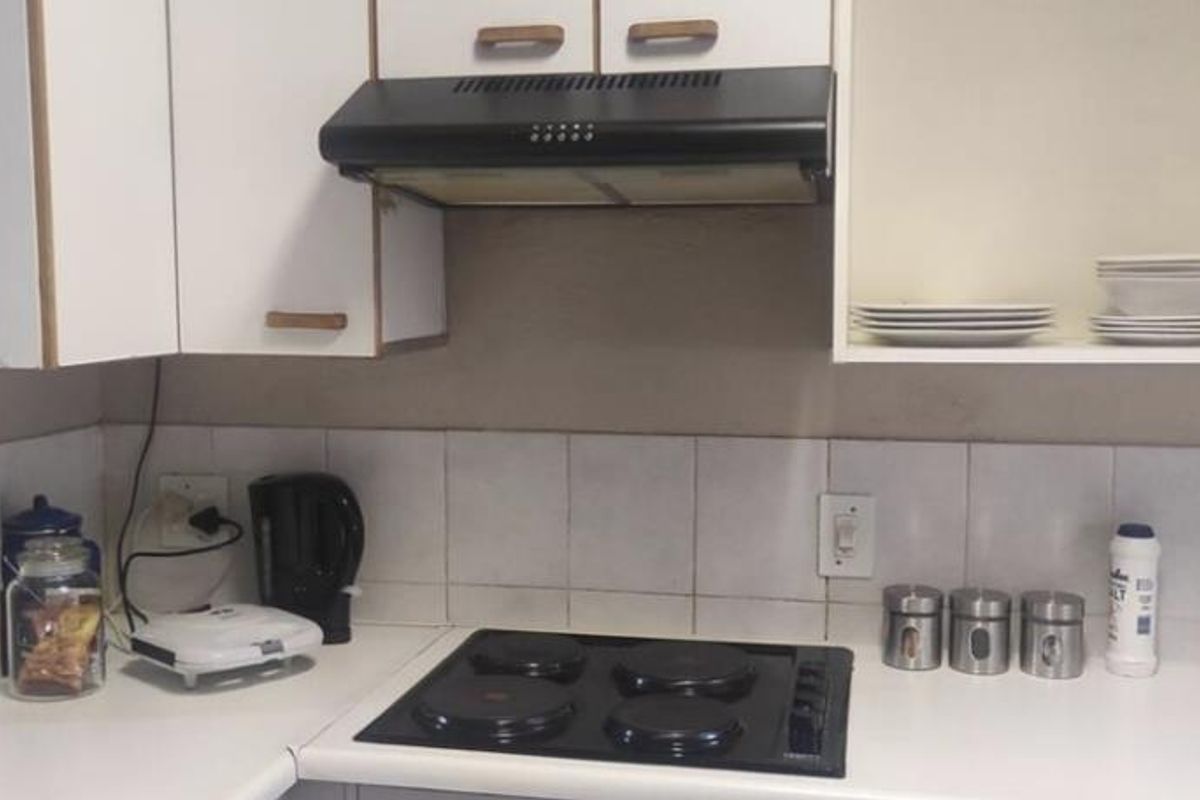 A functional kitchen area featuring white cabinetry, a black electric hob, an extractor fan, and a tiled backsplash.