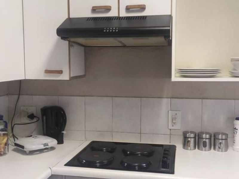 A functional kitchen area featuring white cabinetry, a black electric hob, an extractor fan, and a tiled backsplash.