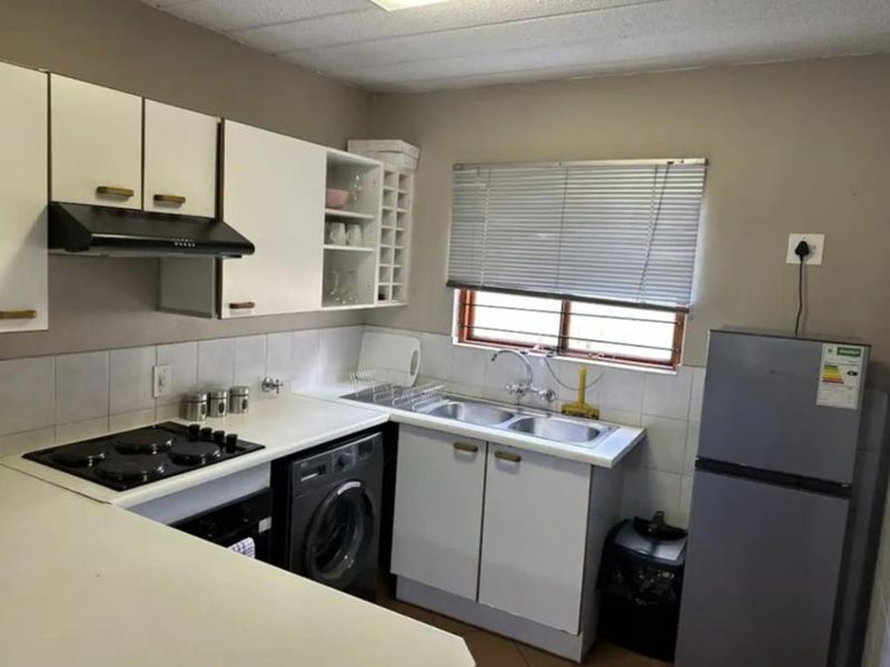 A functional kitchen featuring built-in cabinetry, an electric hob with extractor fan, and a double sink with tiled backsplash.