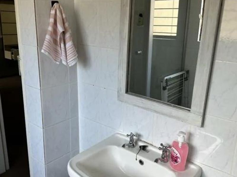 A functional bathroom area featuring a classic pedestal basin with dual taps and a wall-mounted mirror against tiled walls.
