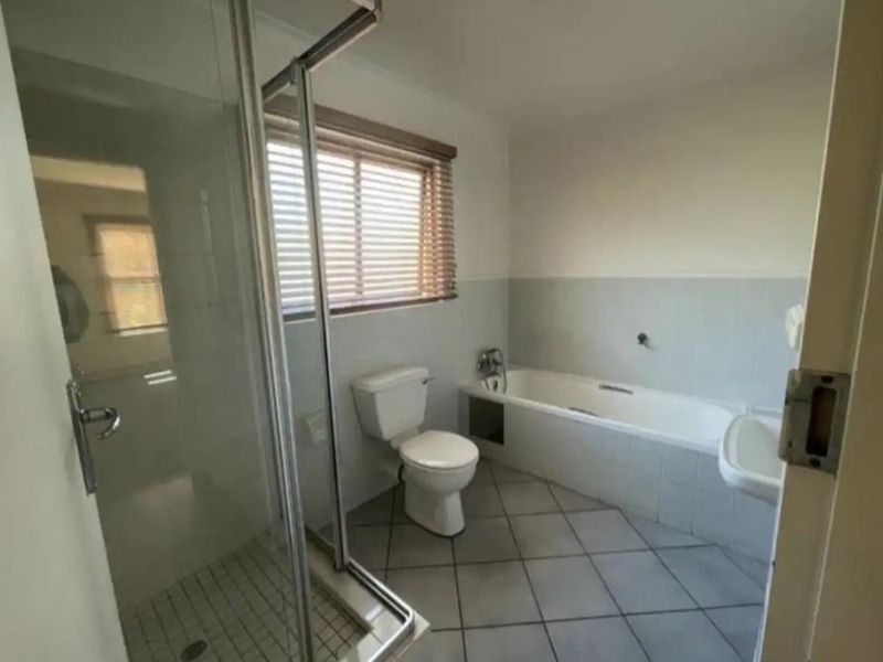 A functional bathroom featuring a glass shower enclosure, a built-in bathtub, a toilet, and a wall-mounted basin with tiled flooring and wall finishes.