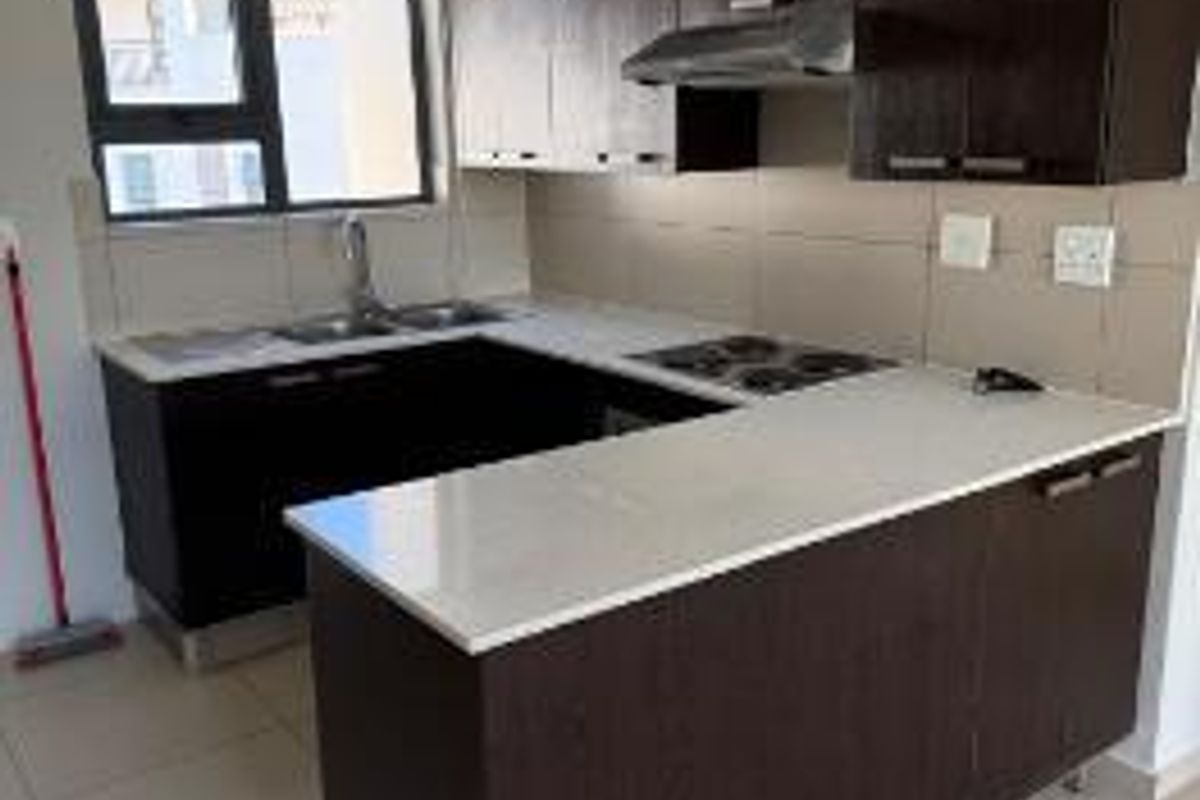 A functional kitchen featuring dark wood cabinetry, stone countertops, an electric hob with extractor fan, and neutral tiled flooring.