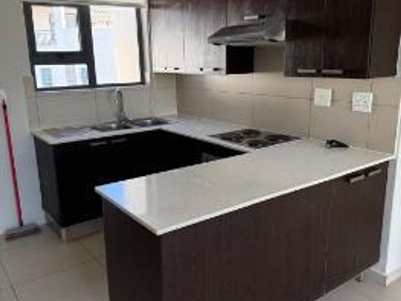 A functional kitchen featuring dark wood cabinetry, stone countertops, an electric hob with extractor fan, and neutral tiled flooring.
