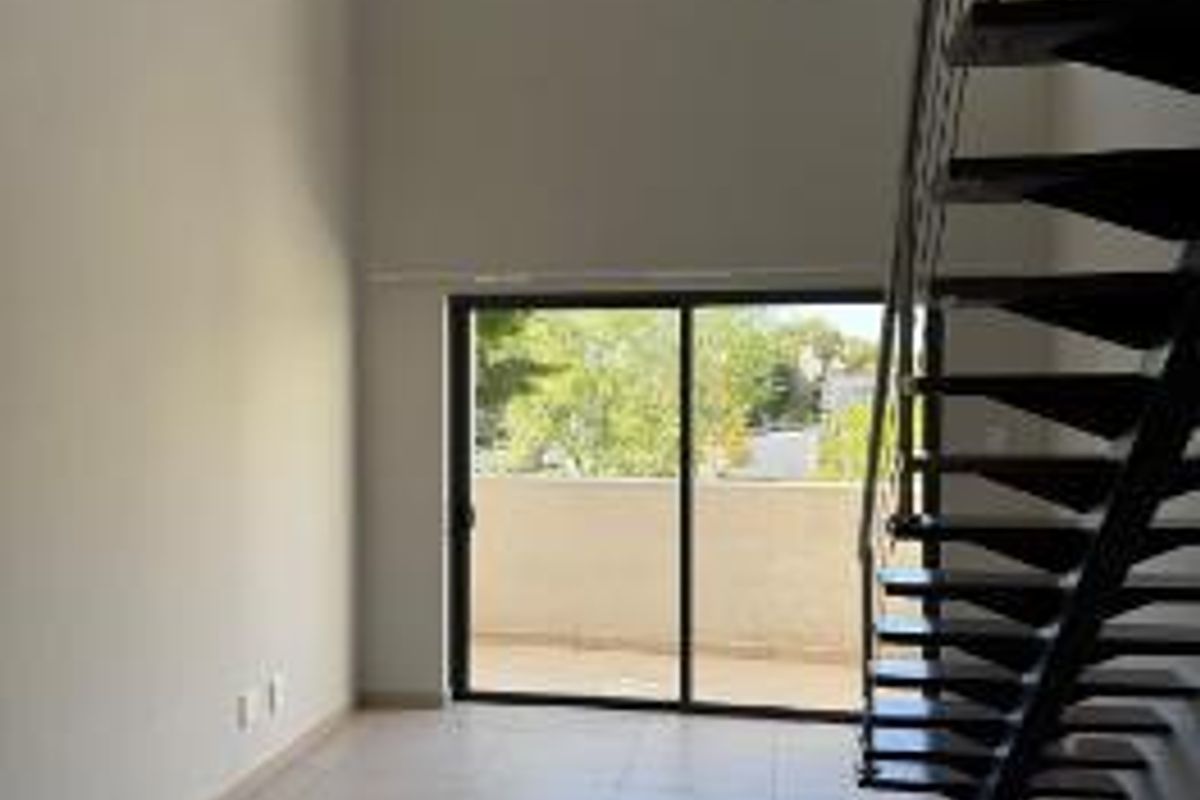 Spacious living area featuring high vaulted ceilings, tiled flooring, a modern metal staircase, and large sliding glass doors leading to a balcony.