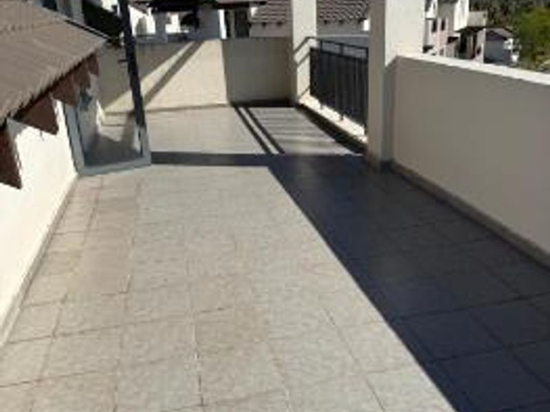 A spacious, covered balcony featuring tiled flooring and a metal balustrade, offering an open outdoor area accessible through a glass door.