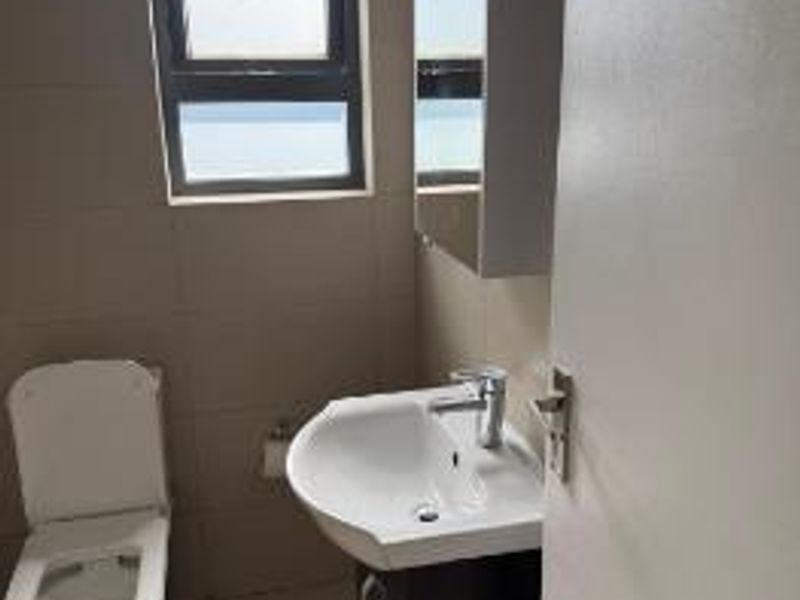 A clean and functional bathroom featuring a modern vanity basin, toilet, and tiled finishes, providing a neutral space ready for personal touches.