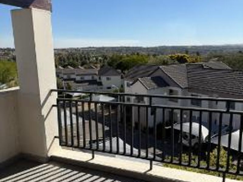 A covered balcony featuring a metal balustrade and tiled flooring, offering an elevated view of the surrounding residential complex.