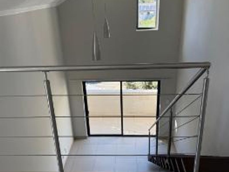 A bright landing area featuring a modern stainless steel cable balustrade, high ceilings, and a sliding door leading to an outdoor space.