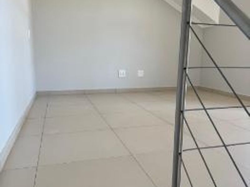 An empty loft-style bedroom area featuring tiled flooring, a sloped ceiling, and a modern metal staircase railing.