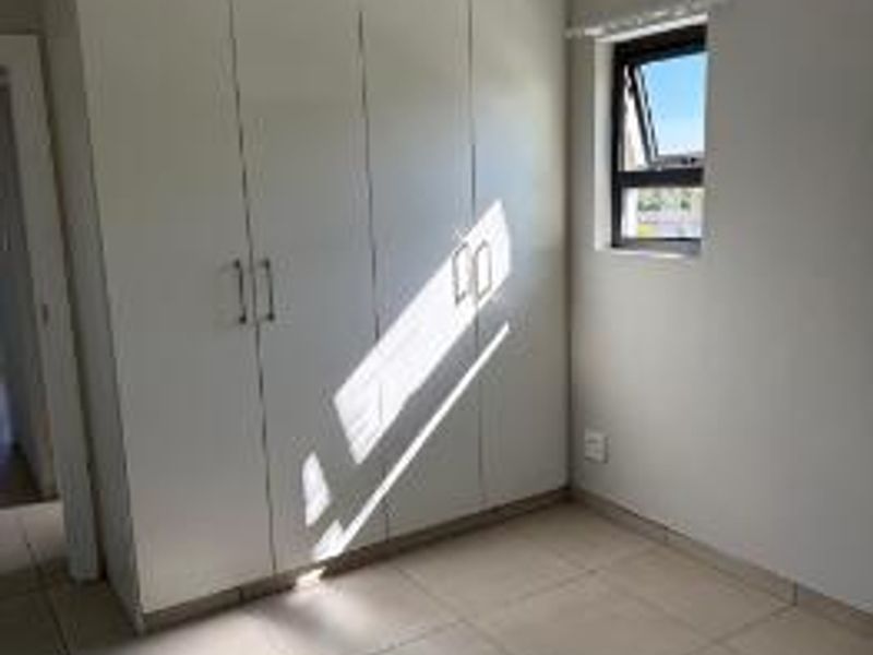 A bright, empty bedroom featuring neutral tiled flooring, built-in white cupboards, and a single window providing natural light.