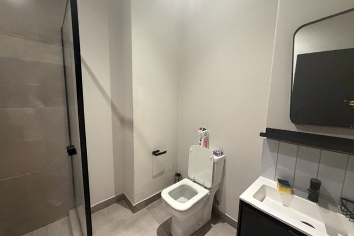 Modern bathroom featuring a walk-in shower with black-framed glass screen, wall-mounted toilet, and a sleek vanity with integrated basin and black fixtures.