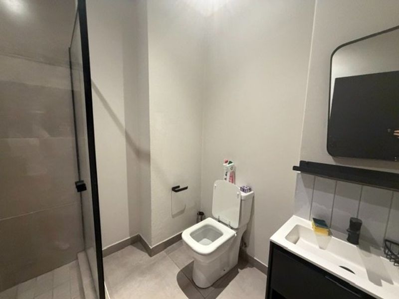 Modern bathroom featuring a walk-in shower with black-framed glass screen, wall-mounted toilet, and a sleek vanity with integrated basin and black fixtures.
