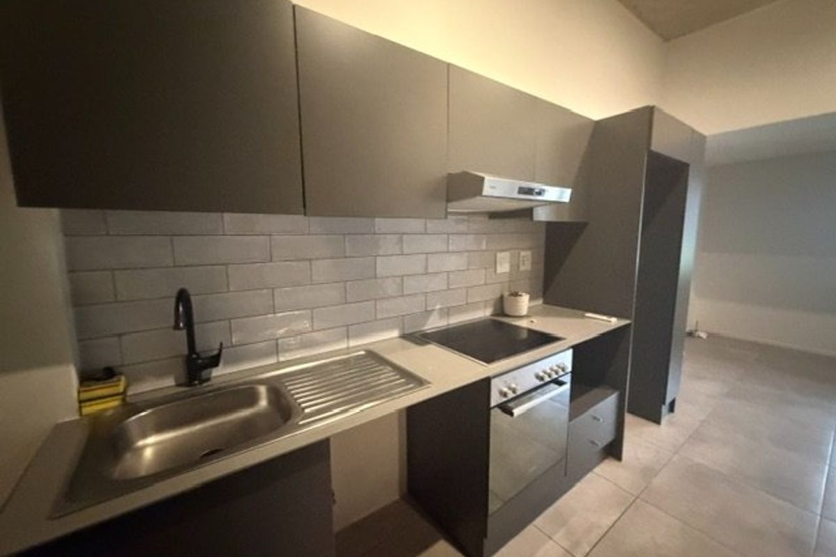 Modern kitchen featuring dark grey cabinetry, subway tile backsplash, stainless steel sink, and integrated electric oven and hob.
