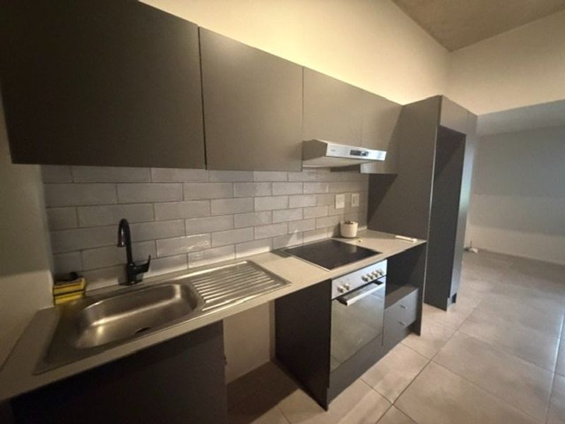 Modern kitchen featuring dark grey cabinetry, subway tile backsplash, stainless steel sink, and integrated electric oven and hob.