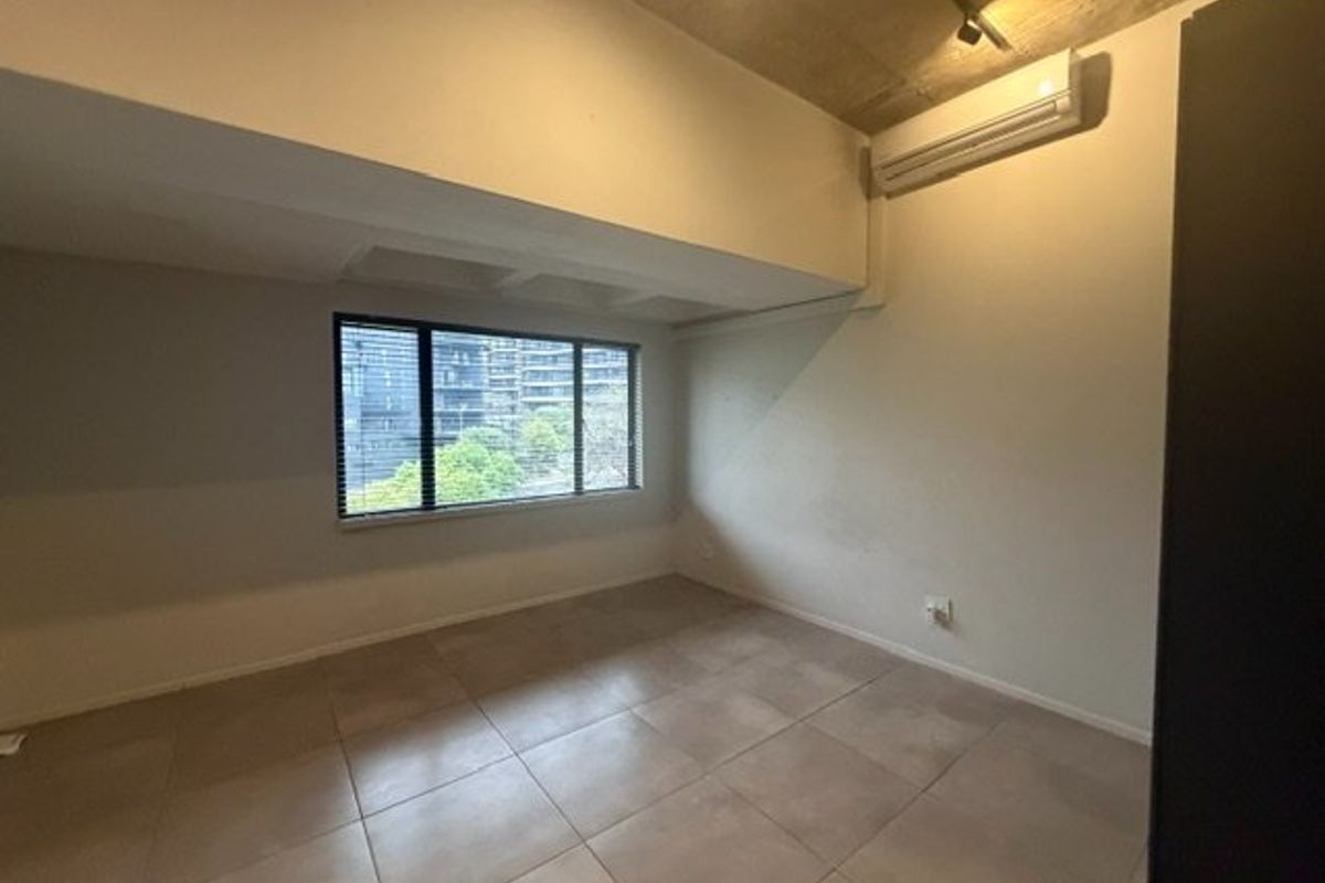 An empty bedroom featuring tiled flooring, an exposed concrete ceiling, and a wall-mounted split-system air conditioner with views through a window.