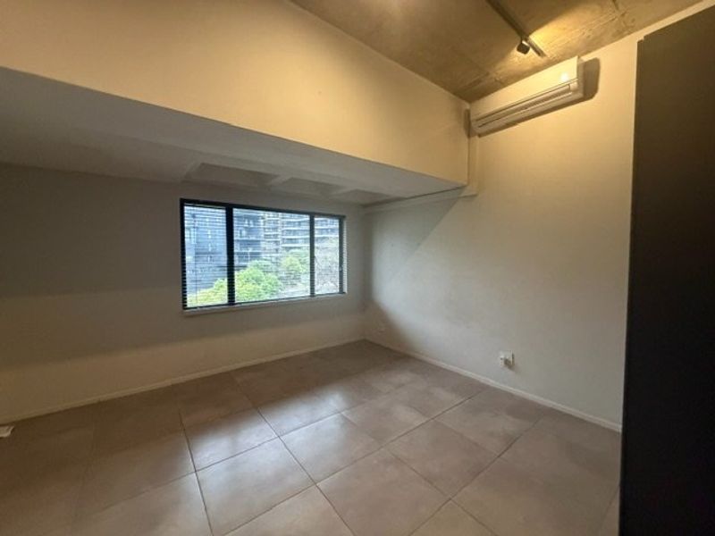 An empty bedroom featuring tiled flooring, an exposed concrete ceiling, and a wall-mounted split-system air conditioner with views through a window.
