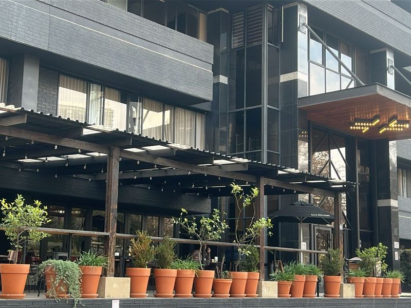 Modern apartment building exterior featuring a covered patio area with timber pergola, glass facade, and contemporary brick cladding.