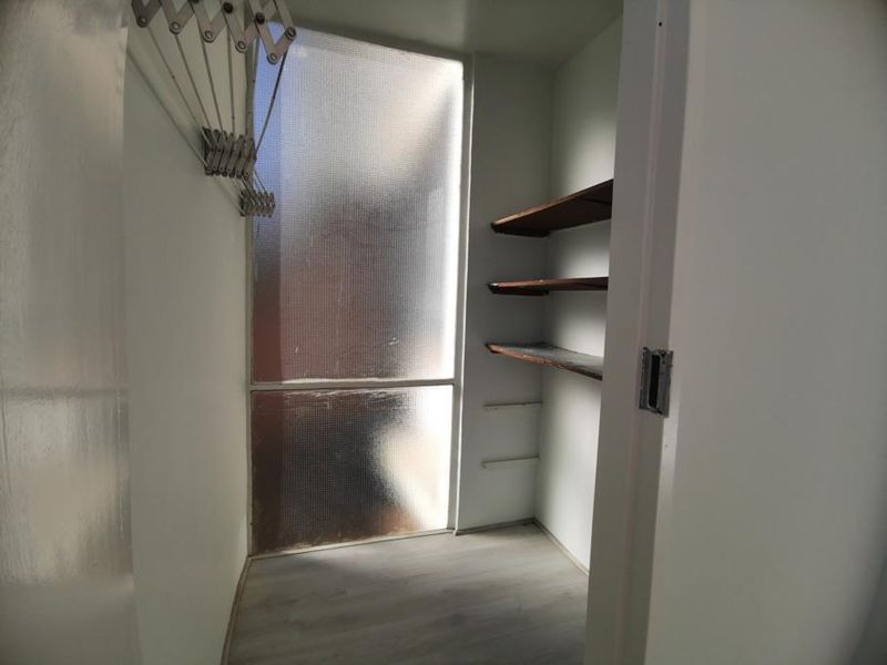 A functional utility or storage space featuring built-in shelving, a wall-mounted drying rack, and a textured glass window for natural light.