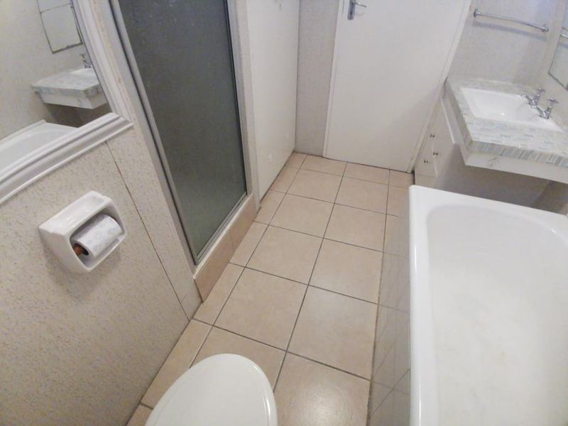 A functional bathroom featuring a shower enclosure, bathtub, vanity basin, and tiled flooring, offering a clean but dated aesthetic ready for modernization.