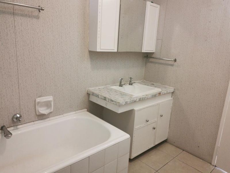 A dated bathroom featuring a built-in vanity with a medicine cabinet, a bathtub, and tiled flooring, offering potential for modernization and renovation.