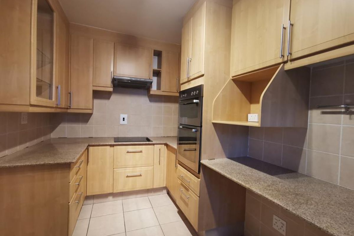 A clean, functional kitchen featuring light wood cabinetry, granite countertops, a double wall oven, and an electric hob with a tiled backsplash.