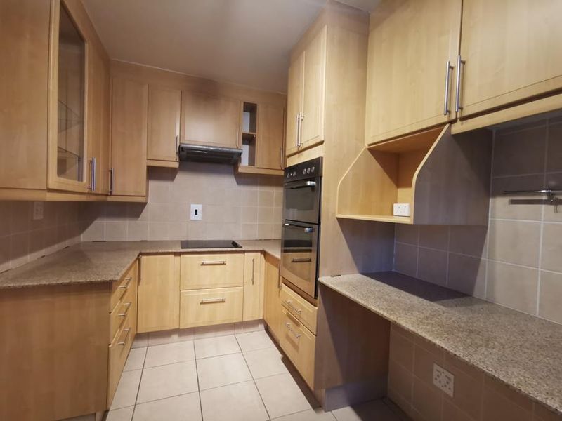A clean, functional kitchen featuring light wood cabinetry, granite countertops, a double wall oven, and an electric hob with a tiled backsplash.